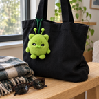 Green alien cat bag charm hanging from a black tote bag handle