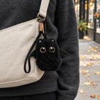 Black bat cat charm clipped to a beige crossbody bag on an autumn sidewalk