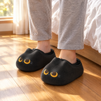 Black Cat Mule Slippers worn on a wooden bedroom floor beside the bed in morning light