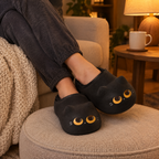 Black Cat Mule Slippers worn with ankles crossed on a footstool in warm lamp light
