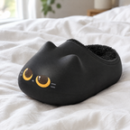 Close-up of a black cat mule slipper on white linen bedding showing its face and texture