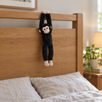 Black monkey plush hanging from a wooden headboard above a made bed