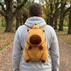 Adult wearing the capybara plush backpack on a park path, seen from behind