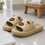 Pair of beige capybara slide sandals on a bathroom floor next to a bath mat