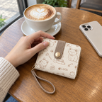 Cat doodle wallet on a cafe table next to a cappuccino and an adult hand