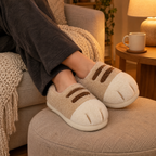 Beige Cat Paw Slippers worn with ankles crossed on a footstool in warm lamp light