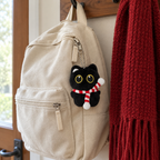 Black cat keychain with a striped scarf clipped to a backpack zipper