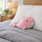 Chubby pink whale plush resting on the pillows of a made bed