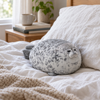 Grumpy spotted seal plush sitting on a made bed against a pillow