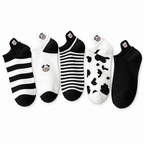 Five pairs of black and white cow ankle socks laid flat on a white background