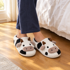 Black and White Cow Face House Slippers worn on a wooden bedroom floor beside the bed in morning light