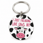 Round cow-print keychain with a cartoon cow face on a silver ring, on a white background