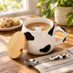 Cow mug with milky coffee, lid and spoon on a wooden table