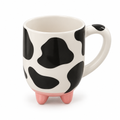 Cow print ceramic mug with pink feet on a white background