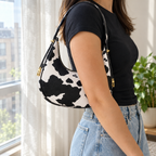 Adult wearing the cow print half-moon shoulder bag under one arm