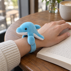 Sky blue plush dolphin hugging an adult wrist over an open book