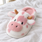 Close-up of a pink fluffy cow slide slipper on white linen bedding showing its muzzle, ears and horns