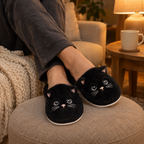Black Fuzzy Cat Slippers worn with ankles crossed on a footstool in warm lamp light