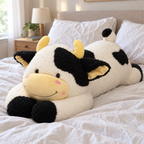 Giant black-and-white cow plush lying along a made bed