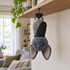 Gray bat plush hanging upside down from a hook under a wooden shelf