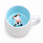 White ceramic mug with a tiny 3D cow figurine inside, on a white background
