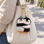 Hugging penguin bag charms clipped to a cream shoulder bag outdoors