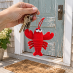 Red lobster plush keychain on house keys held in a hand by a beach-house door