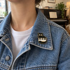 Black cat piano enamel pin on the collar of a denim jacket