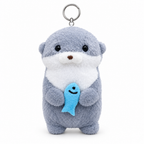 Blue gray otter plush keychain hugging a blue fish on a white background