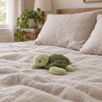 Sage green turtle plush resting on a made bed