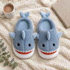 Dusty Blue Shark Plush Slippers flat lay on a knit blanket with cocoa, a book and greenery