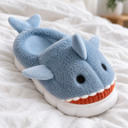 Close-up of a dusty blue shark plush slipper's fluffy face and toothy grin on white bedding