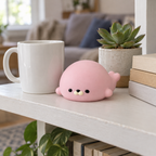 Pink seal squishy on a bookshelf next to a mug and a small plant