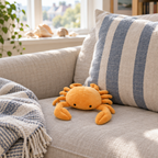 Orange crab plush sitting on a linen sofa in a sunny living room
