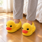 Yellow Duck Plush Slippers worn on a wooden bedroom floor beside the bed in morning light
