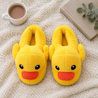 Yellow Duck Plush Slippers flat lay on a knit blanket with cocoa, a book and greenery